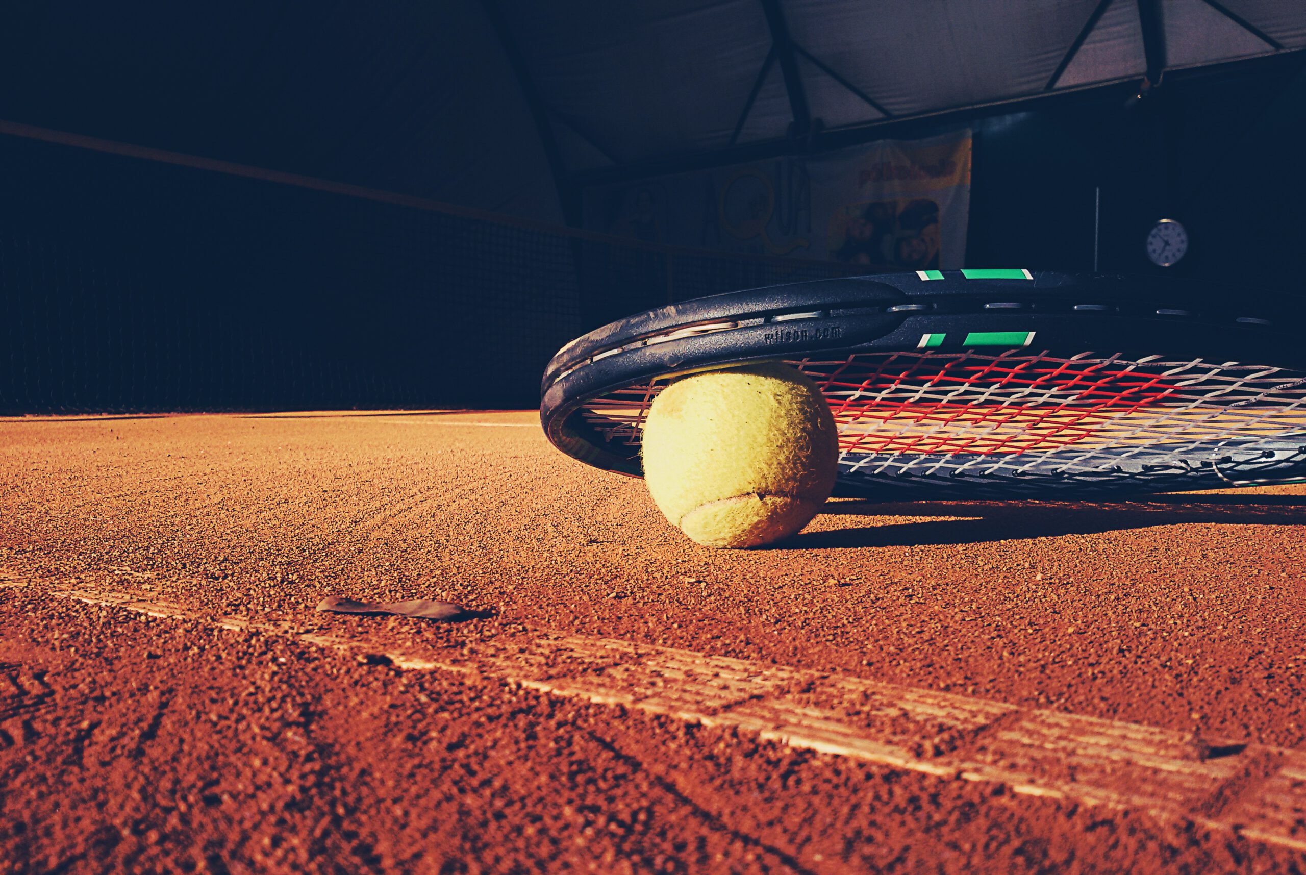 Pelota de tenis debajo de una raqueta en el suelo de una pista de tennis.